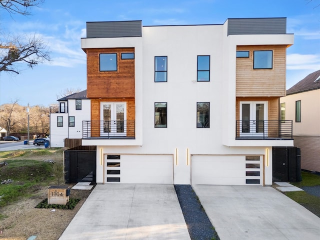 view of front facade with stucco siding, french doors, concrete driveway, an attached garage, and a balcony