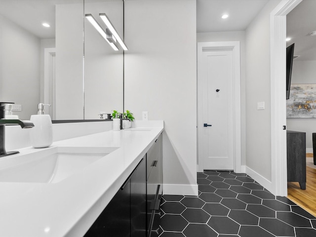 bathroom with double vanity, recessed lighting, baseboards, and a sink