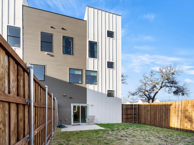 rear view of house featuring a lawn, board and batten siding, a fenced backyard, and a patio