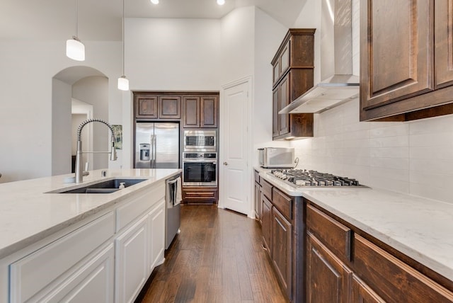 kitchen with dark wood-type flooring, a sink, backsplash, stainless steel appliances, and wall chimney exhaust hood