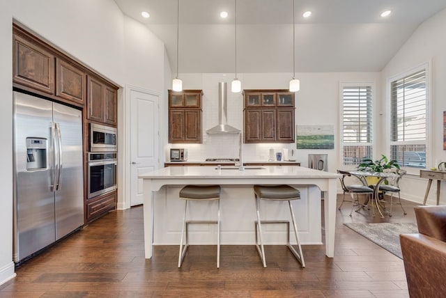 kitchen featuring dark wood finished floors, stainless steel appliances, light countertops, wall chimney exhaust hood, and tasteful backsplash