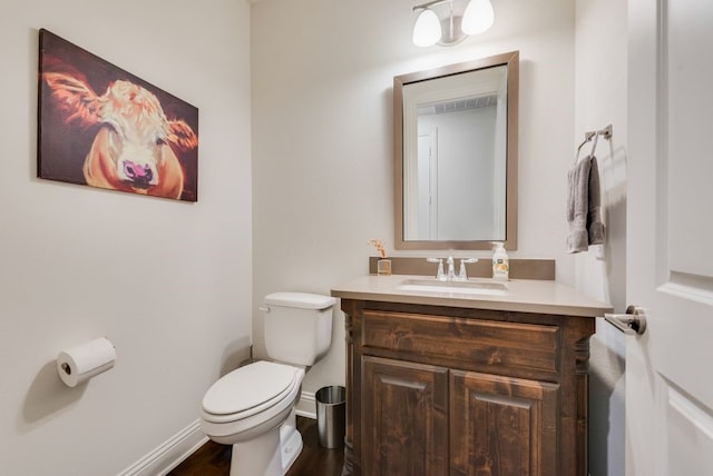 half bath featuring visible vents, toilet, wood finished floors, baseboards, and vanity