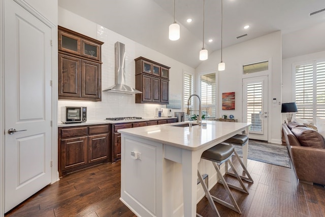 kitchen with a center island with sink, a sink, wall chimney exhaust hood, light countertops, and stainless steel gas cooktop