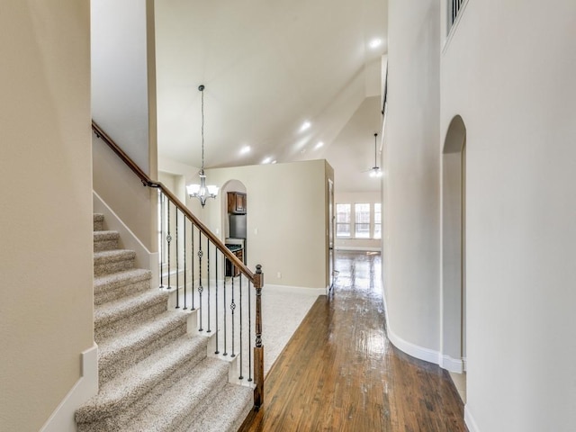 staircase with arched walkways, baseboards, an inviting chandelier, and hardwood / wood-style floors