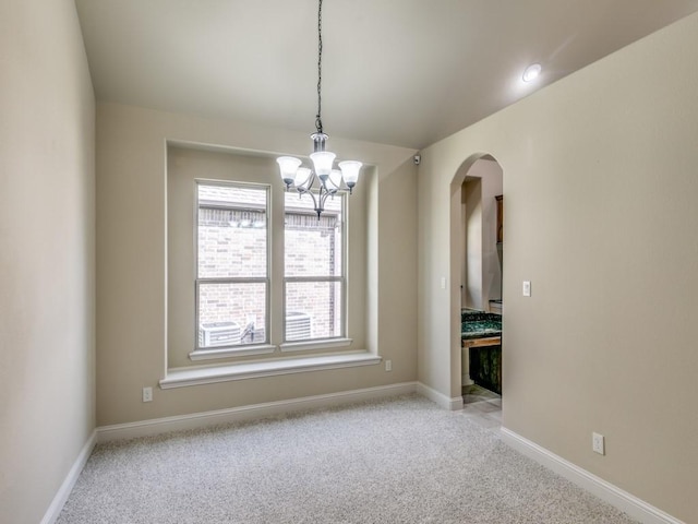 empty room with light carpet, a notable chandelier, arched walkways, and baseboards