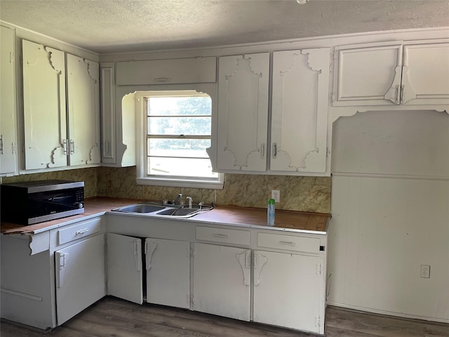 kitchen with a sink, stainless steel microwave, a textured ceiling, and wood finished floors