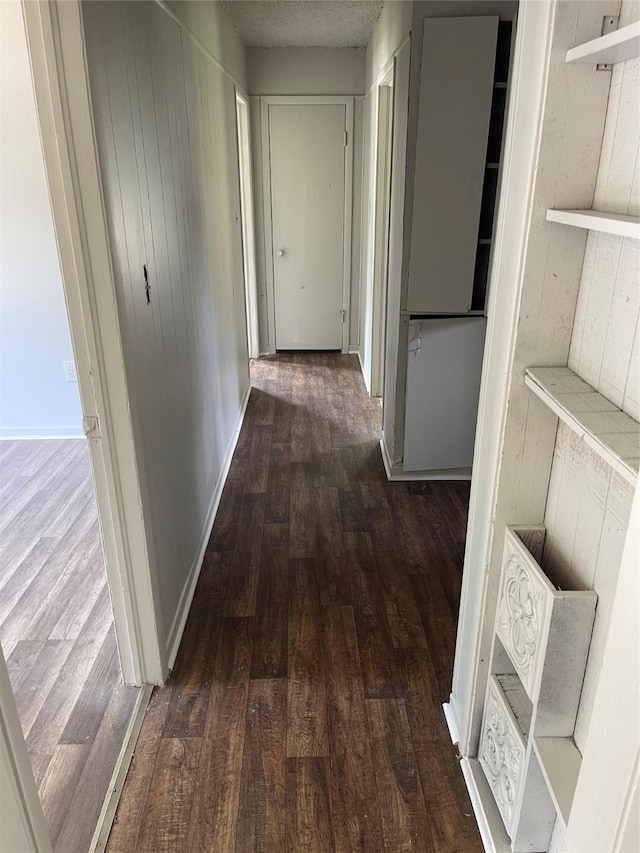 corridor featuring wood finished floors, baseboards, and a textured ceiling