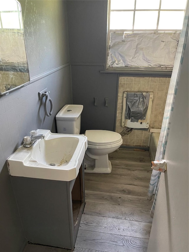 bathroom featuring toilet, heating unit, wood finished floors, tile walls, and vanity