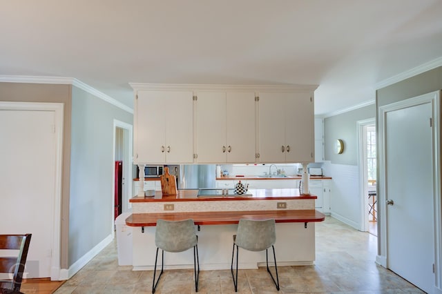 kitchen featuring baseboards, ornamental molding, a kitchen breakfast bar, white cabinetry, and a sink