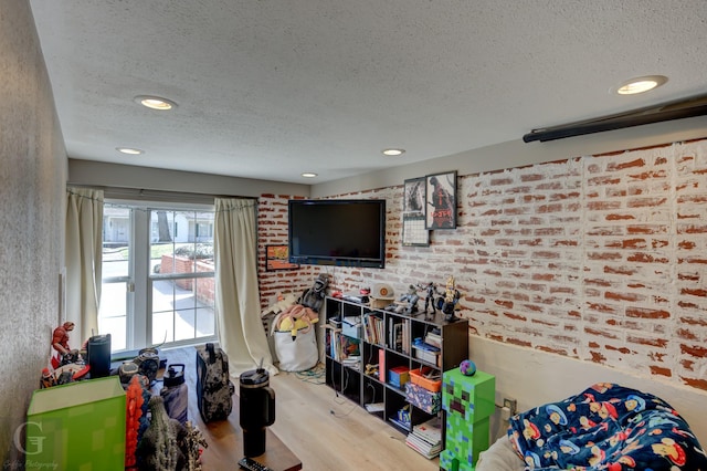 rec room featuring recessed lighting, brick wall, a textured ceiling, and wood finished floors