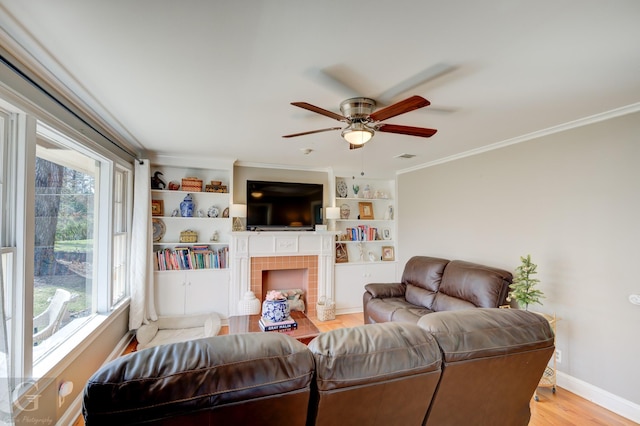 living room with light wood-type flooring, ornamental molding, a fireplace, baseboards, and ceiling fan