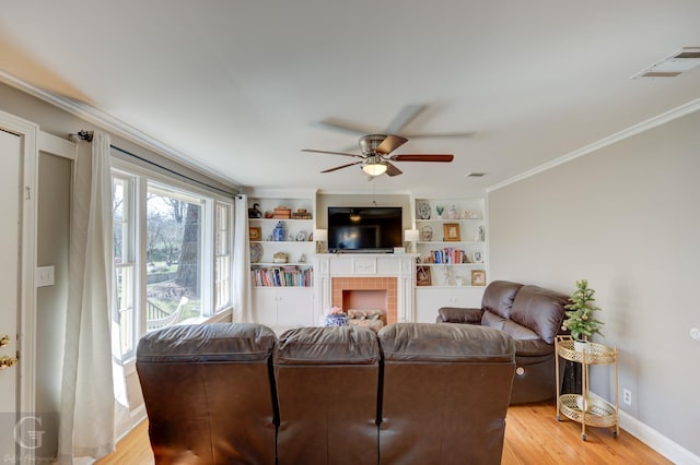 living room featuring light wood-type flooring, visible vents, a fireplace, crown molding, and baseboards