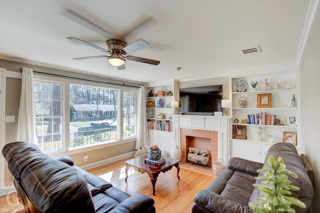 living area featuring visible vents, ceiling fan, ornamental molding, a tile fireplace, and wood finished floors