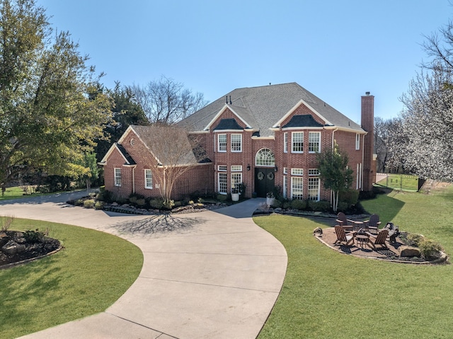 colonial home with driveway, a front lawn, a patio, brick siding, and a chimney