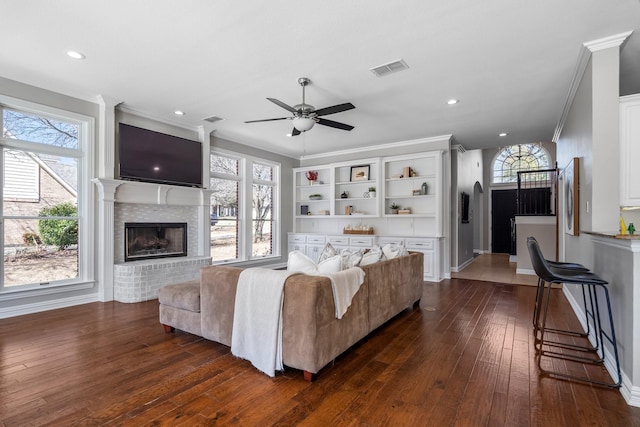 living area featuring crown molding, a brick fireplace, a healthy amount of sunlight, and dark wood-style flooring