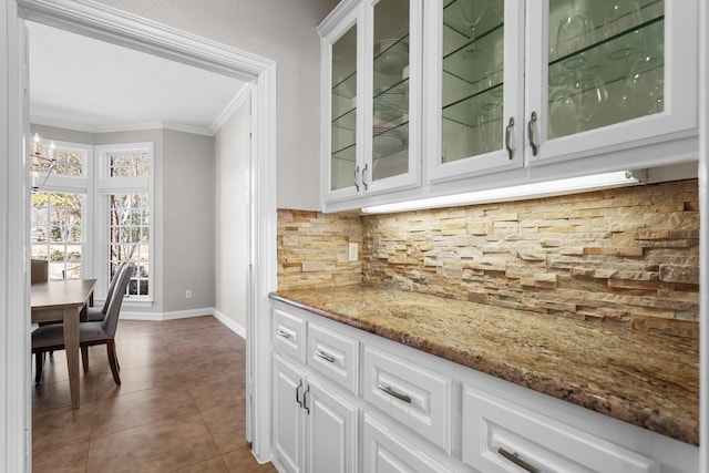 kitchen with dark tile patterned flooring, ornamental molding, tasteful backsplash, white cabinets, and glass insert cabinets