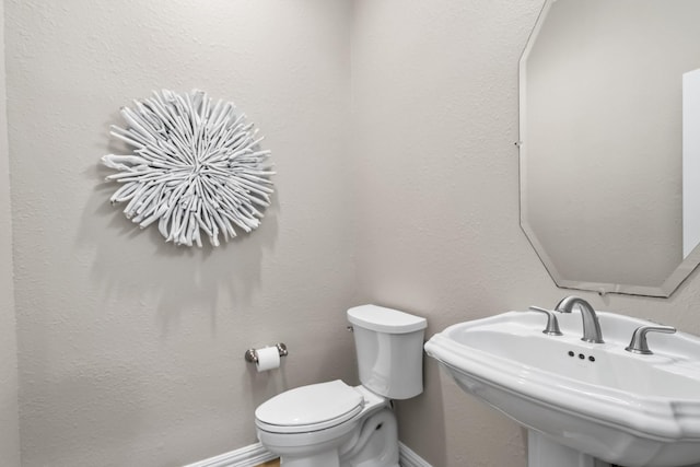 half bath with toilet, baseboards, and a sink