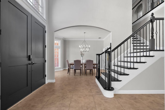 foyer with crown molding, baseboards, stairs, a towering ceiling, and arched walkways