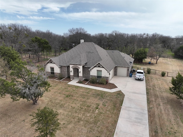 view of front of property featuring stone siding, fence, concrete driveway, a shingled roof, and a chimney