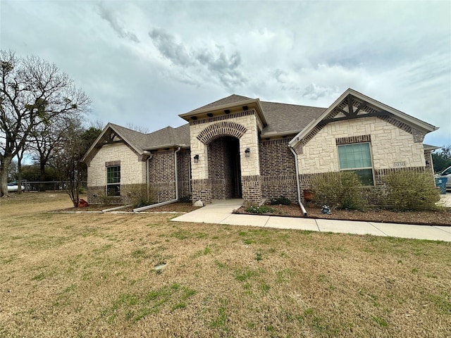 french country style house featuring a front lawn, brick siding, stone siding, and a shingled roof