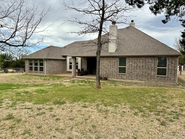 rear view of house featuring a patio, a yard, brick siding, and roof with shingles