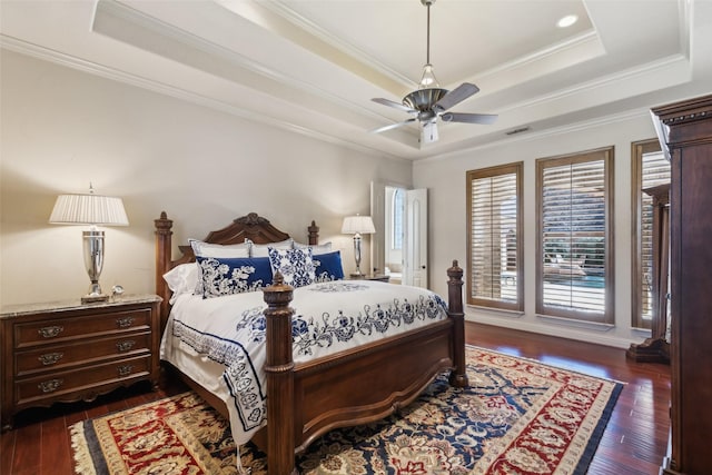 bedroom with dark wood finished floors, a tray ceiling, crown molding, and visible vents