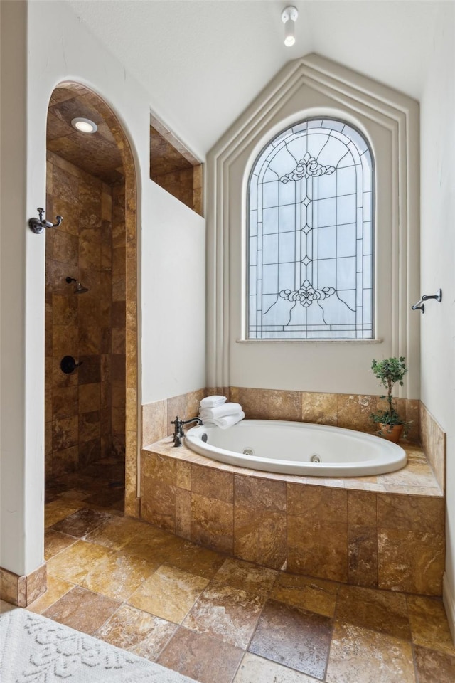 full bath featuring lofted ceiling, stone tile floors, a tub with jets, and tiled shower