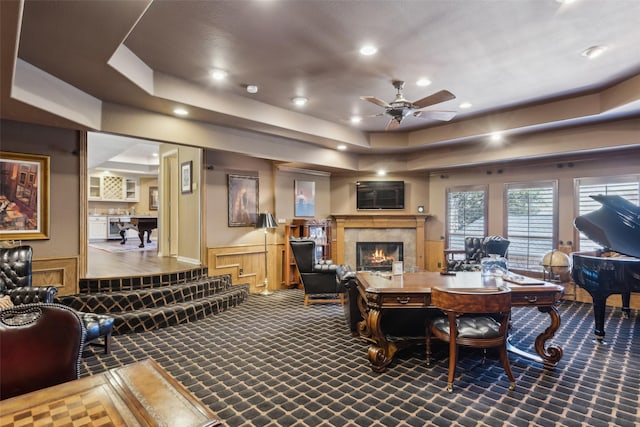 interior space featuring a wainscoted wall, a raised ceiling, ceiling fan, and a tiled fireplace