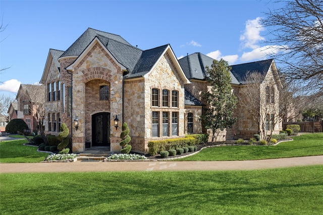 french country home with a front yard, brick siding, and stone siding