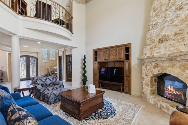 living area featuring french doors, light tile patterned flooring, a fireplace, stairs, and ornate columns