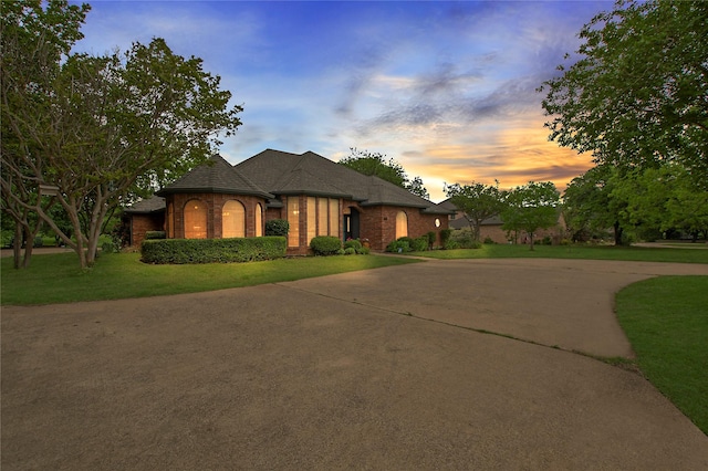 french provincial home featuring a front lawn, concrete driveway, and brick siding