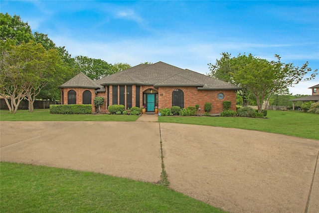 french country home featuring brick siding, concrete driveway, a front lawn, and roof with shingles