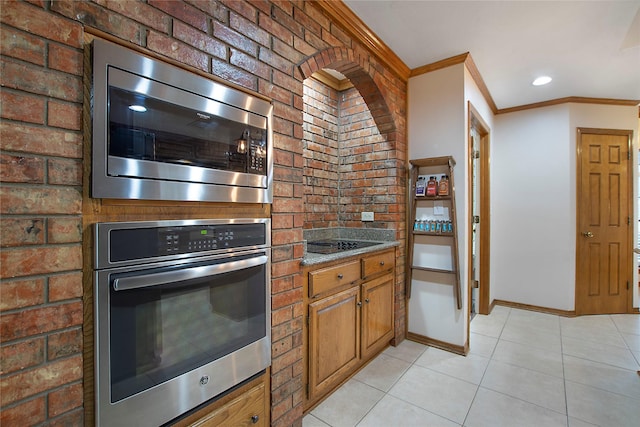 kitchen featuring brown cabinets, ornamental molding, stainless steel appliances, light tile patterned flooring, and baseboards