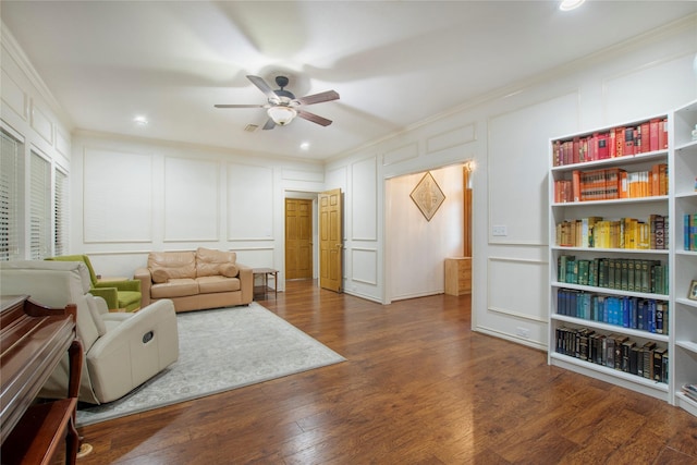 living area featuring dark wood finished floors, a decorative wall, crown molding, and a ceiling fan