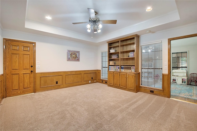 living area featuring wainscoting, a raised ceiling, ornamental molding, and carpet floors