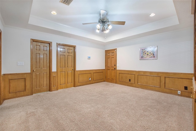 unfurnished bedroom featuring a raised ceiling, ornamental molding, carpet floors, and wainscoting