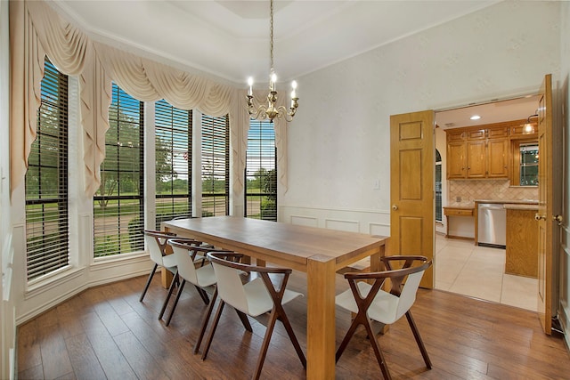 dining room with a tray ceiling, an inviting chandelier, light wood-style flooring, and wainscoting