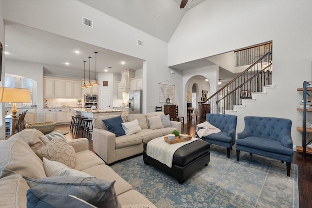 living room with dark wood finished floors, visible vents, arched walkways, and stairs