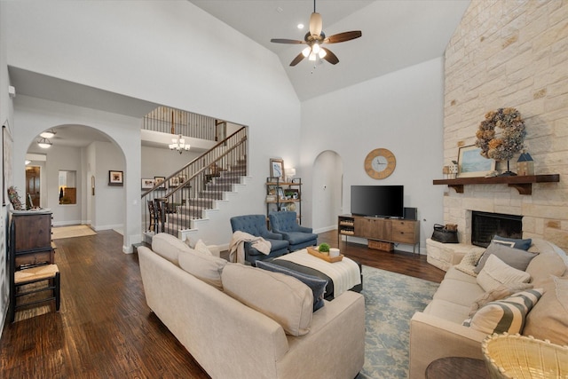 living area featuring wood finished floors, a fireplace, arched walkways, stairs, and ceiling fan with notable chandelier