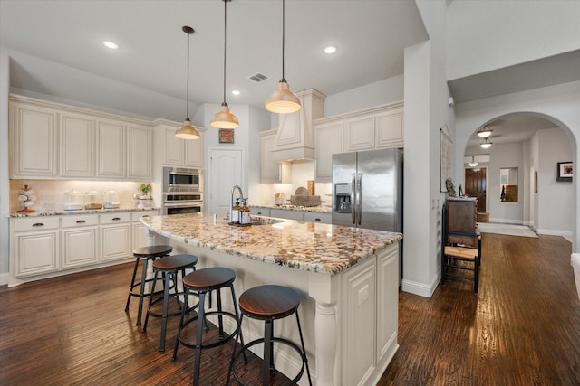 kitchen featuring visible vents, arched walkways, dark wood-style flooring, stainless steel appliances, and backsplash