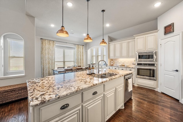 kitchen with decorative light fixtures, light stone counters, dark wood-style floors, stainless steel appliances, and a sink