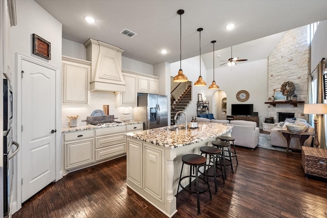 kitchen featuring visible vents, premium range hood, a sink, a stone fireplace, and appliances with stainless steel finishes