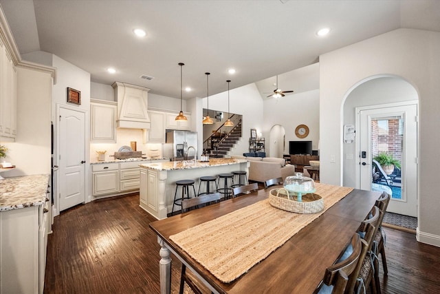 dining area with arched walkways, a ceiling fan, stairs, and lofted ceiling