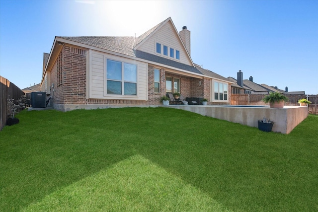 rear view of property with cooling unit, a fenced backyard, a chimney, a lawn, and brick siding