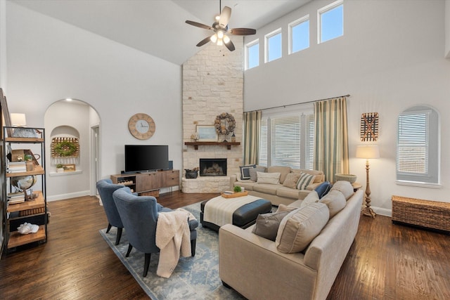 living area with dark wood-style floors, baseboards, a ceiling fan, a fireplace, and arched walkways