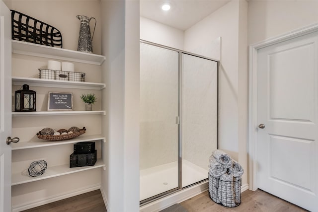 bathroom with baseboards, wood finished floors, and a shower stall