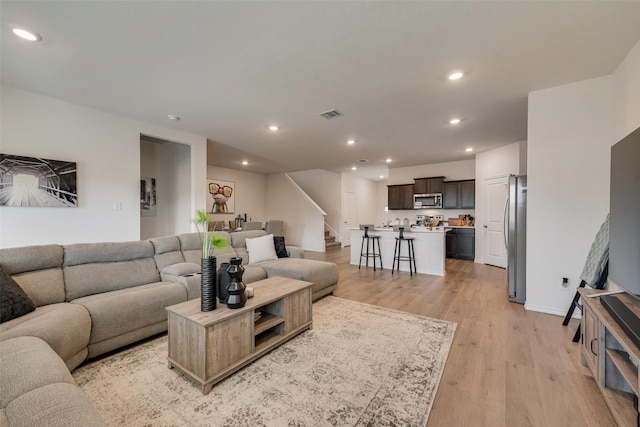 living area featuring visible vents, baseboards, stairs, recessed lighting, and light wood-style flooring