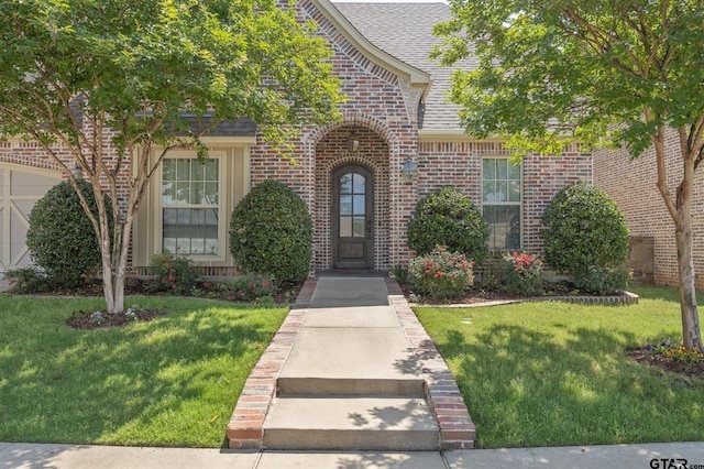 entrance to property featuring brick siding, a lawn, and a shingled roof