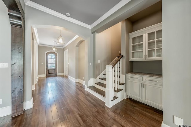 foyer featuring dark wood-type flooring, ornamental molding, arched walkways, baseboards, and stairs