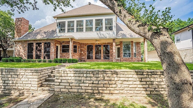 rear view of property featuring a ceiling fan, roof with shingles, a chimney, a lawn, and brick siding